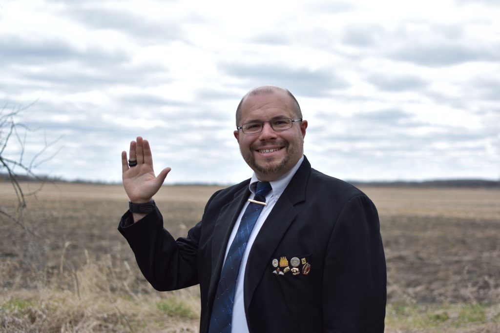 Daniel waving in front of a farmer's field.